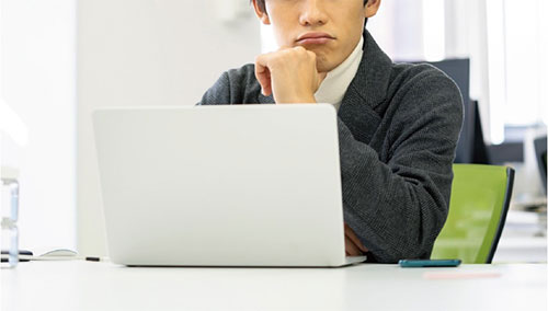 男性がパソコンの前でマンション住居者へのいい案内方法がないか考えている